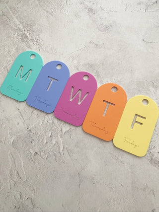 Colourful tags labeled with days of the week on a textured surface