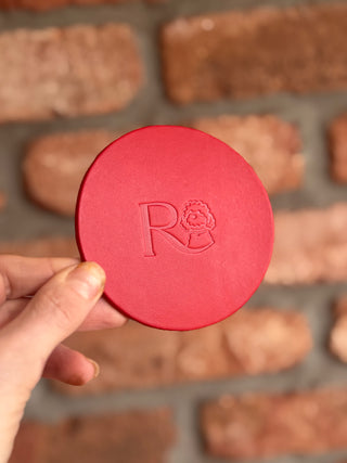 Red leather circular coaster with a logo debossed on it, held by a hand