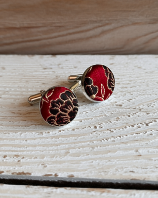 Red cufflinks with black floral pattern on a wooden surface