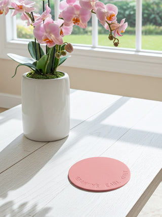 Pink orchid in a white pot on a wooden table with a pink leather personalised coaster stamped with Granny's Earl Grey.