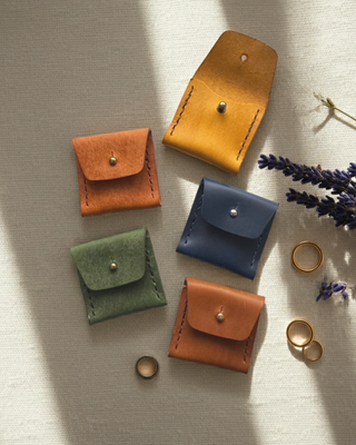 small leather purses in a selection of colours lying on a linen background with gold rings.