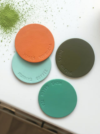 Four round matcha green tea powder containers in different colors on a white surface.