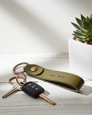 Keychain with keys and 'CAR KEYS' label next to a potted plant on a light surface