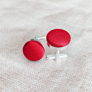 A close-up of a person's hand holding up a red silk cufflink.