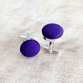 A pair of purple silk covered cufflinks on a textured white background.