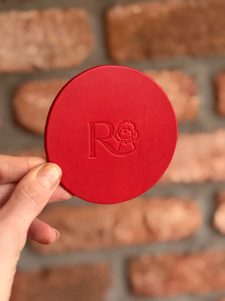 Red circular object with a logo held by a hand, with blurred brown rectangular objects in the background