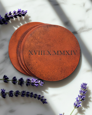 Round tan coasters with engraved text on a marble surface with lavender flowers.