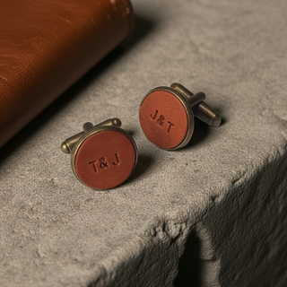 Tan Leather Pair of round cufflinks with 'J&T' engraving on a stone surface.