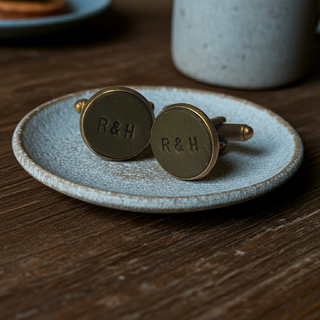 Green Leather cufflinks with 'R&H' engraving on a textured plate, placed on a wooden surface.
