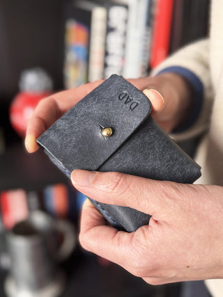 Person holding a dark navy leather wallet with a gold button, blurred background