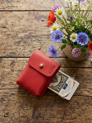 Red deck of cards with cards on a wooden table next to a vase of flowers