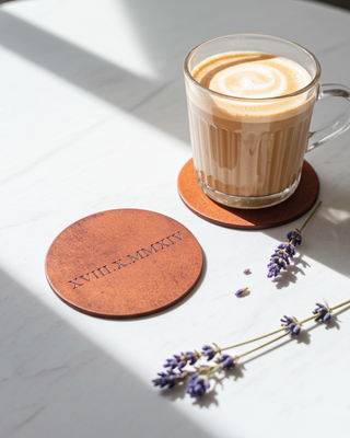 Glass of coffee on a tan leather coaster with lavender flowers on a light surface