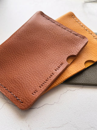 Three leather passport cover holders in tan, yellow and olive green on a light surface.