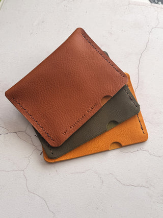 Three leather wallets in tan, green, and yellow on a light white surface.