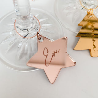 A rose gold star-shaped glass charm with the name 'Eve' engraved on it, hanging from a glass.